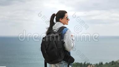 戴墨镜的徒步旅行者女士，背着背包，在<strong>阴雨天</strong>气中欣赏着令人惊叹的海景